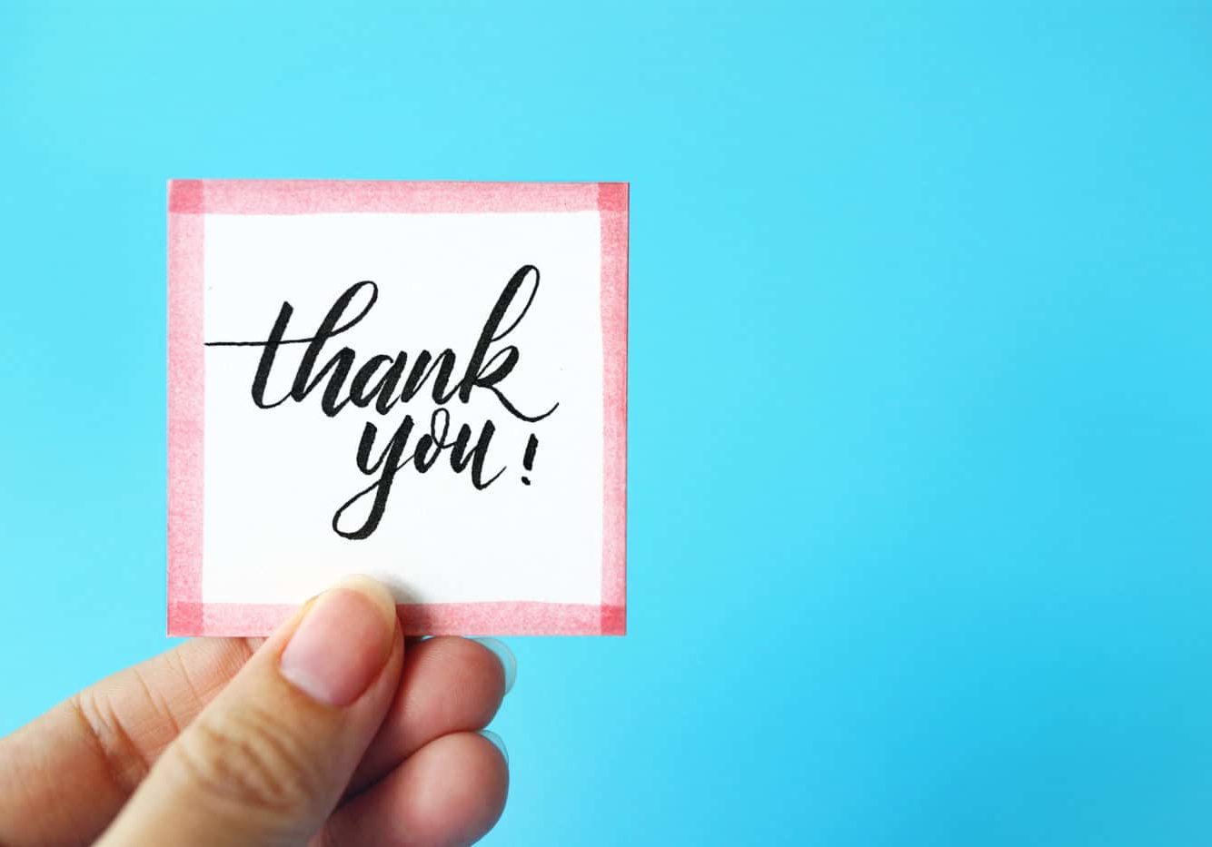 Cropped Hand Holding Thank You Text Against Blue Background Cropped Hand Holding Thank You Text Against Blue Background